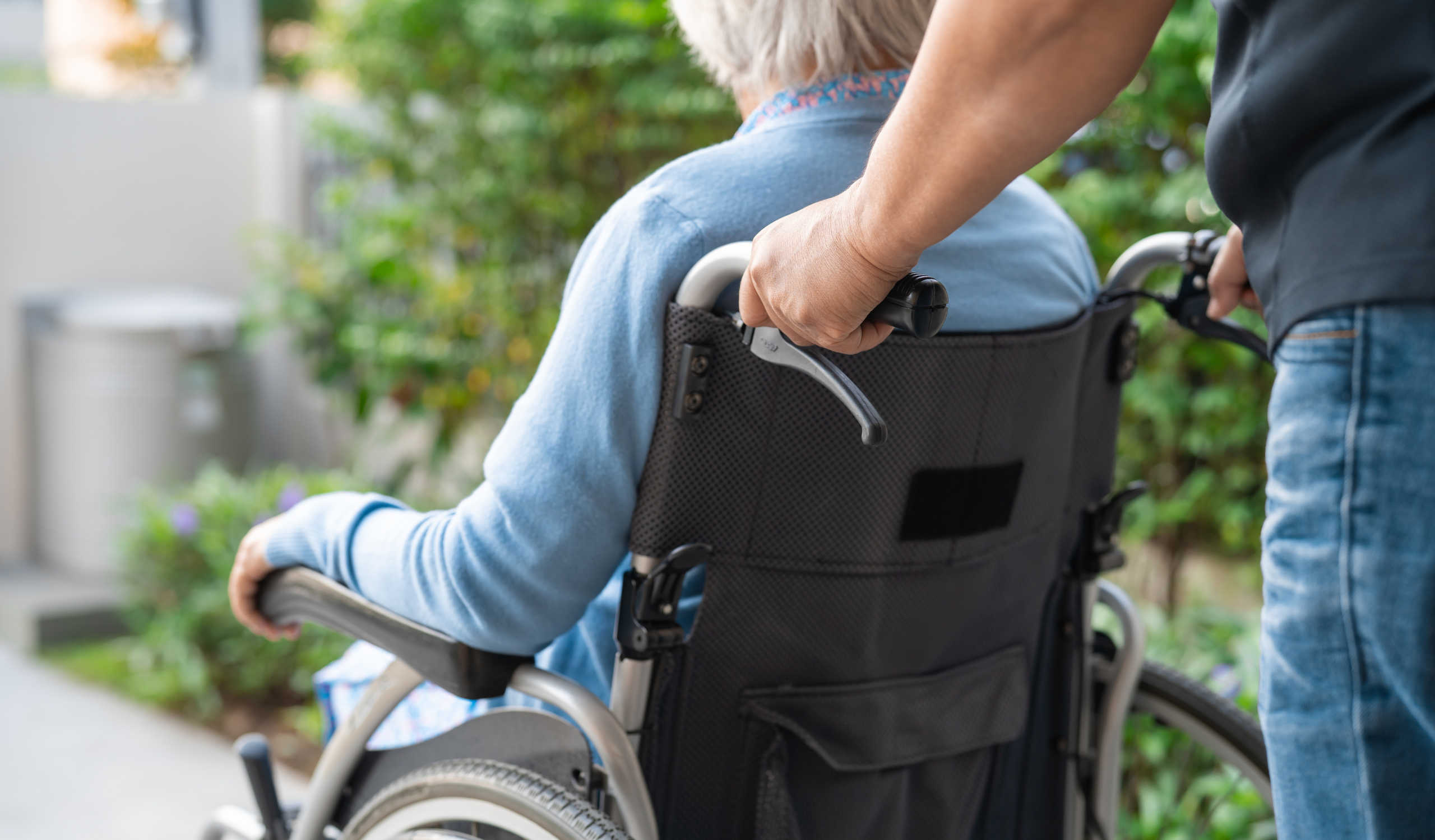 Personne âgée accompagnée en fauteuil roulant par une aide à domicile quelques heures par semaine à Cannes.